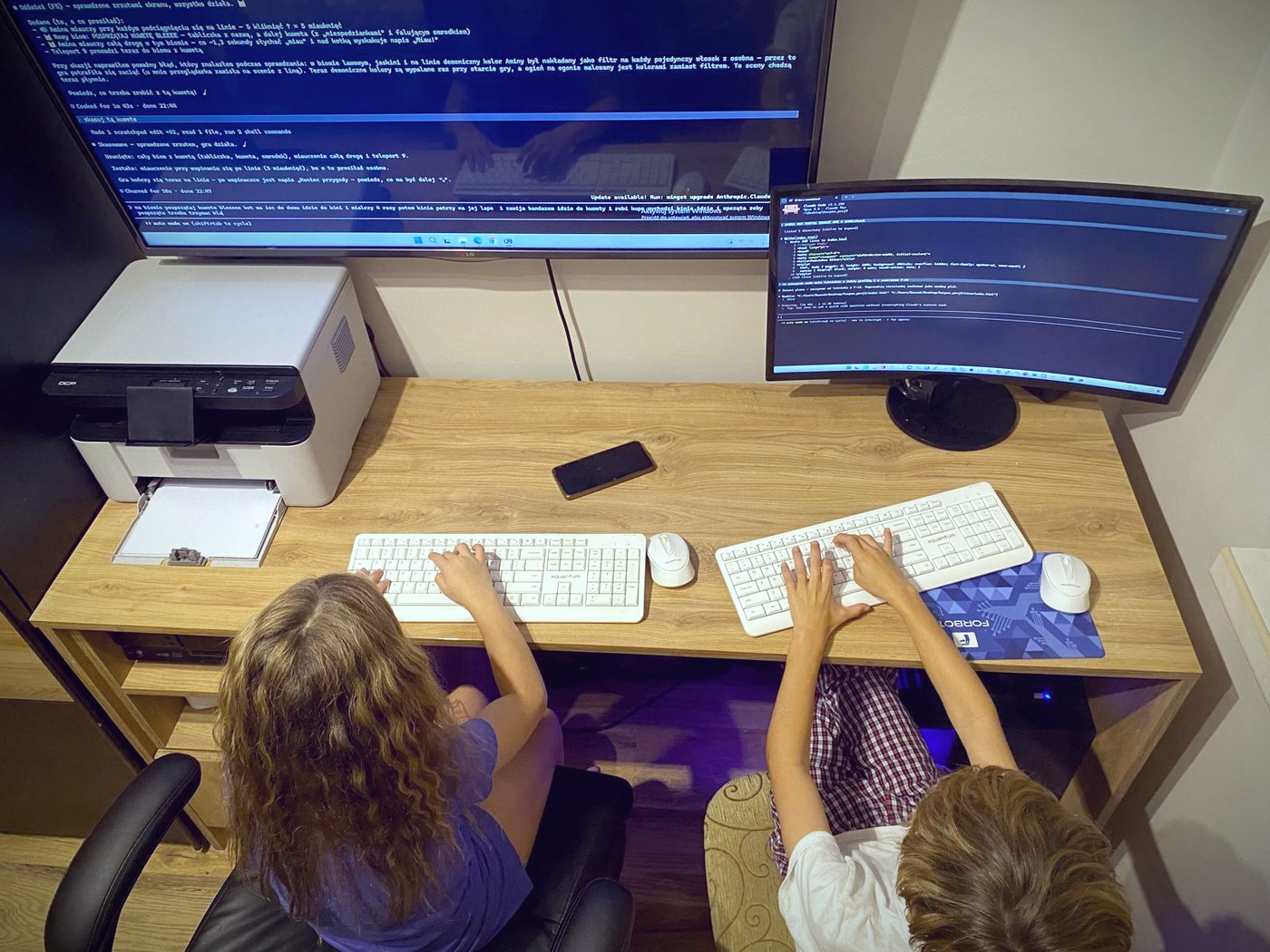 Laura i Kacper przy komputerach tworzą grę z pomocą AI, na monitorach widać Claude Code